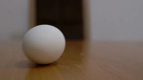 A white chicken egg boiled in the kitchen is spinning quickly on a wooden table Stock Footage 186535992