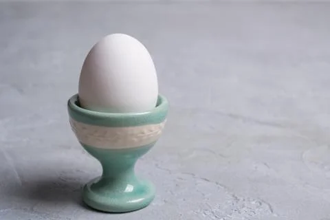White  chicken  egg in ceramic stand. On a gray concrete background. Stock Photos