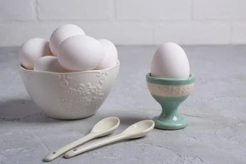 White  chicken  egg in ceramic stand and eggs in white  bowl . On a gray Foto stock