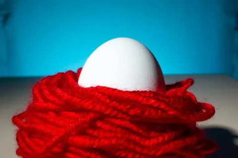 White chicken egg in red threads blue background, close up, copy space Stock Photos
