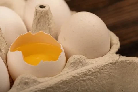 White chicken eggs and one broken egg in a tray made of white cardboard, clos Stock Photos