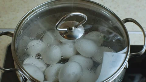 White chicken eggs are boiled in stainless steel saucepan with transparent glass Stock Footage 242381742