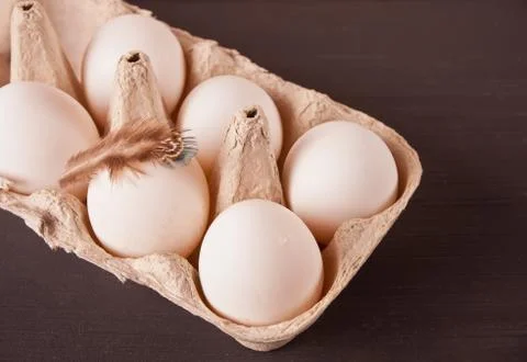 White chicken eggs in egg paper tray with feather on the black background Photos