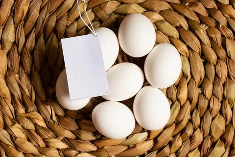 White chicken eggs lying on woven straw with a blank white card on them clo.. Stock Photos