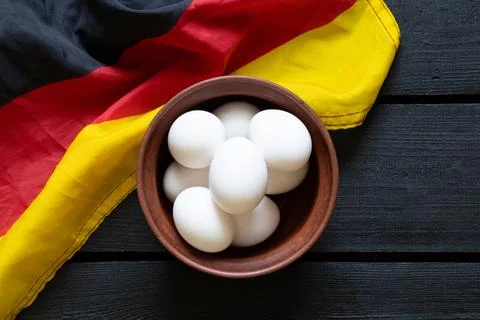 White chicken eggs in a plate next to a German flag on a black wooden table,  Stock Photos