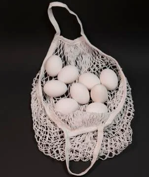 White chicken eggs in a string bag, on a black background Stock Photos