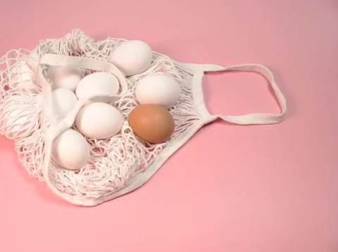 White chicken eggs in a string bag, on a pink background Stock Photos