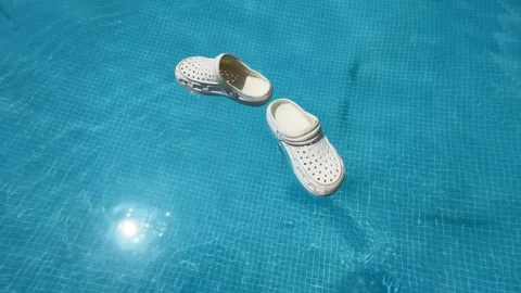 White children's rubber flip-flops float playfully on the sparkling pool surf Video stock 313388966