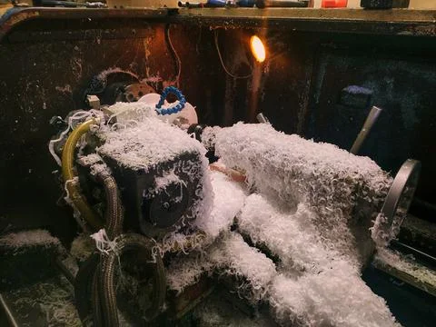 White chips from plastic processing lie on the bed of a cnc lathe Stock Photos