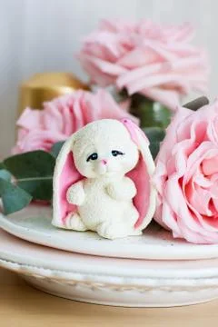 White chocolate tender easter bunny with pink ears. Fresh roses and candle on Stock Photos