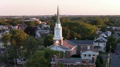 White church steeple with clock face rises above tree-lined neighborhood in New Stock Footage 340969256