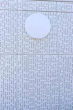 A white circular panel on a perforated wall creates a minimalist architectura Stock Photos