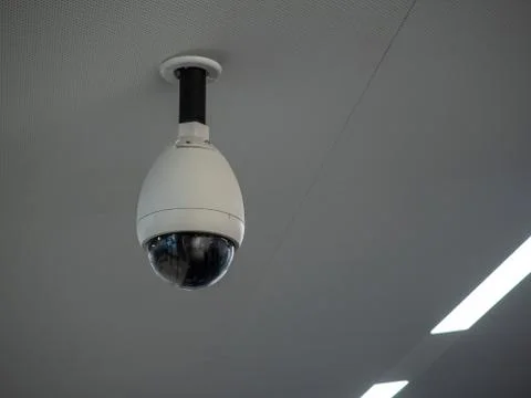 White circular surveillance camera on ceiling in a public setting attached to Stock Photos