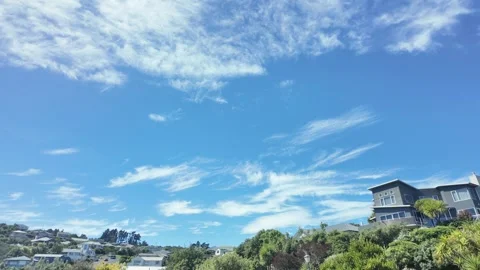 White cirrus clouds dissipating in a blue sky over a residential hill Stock Footage 329343252