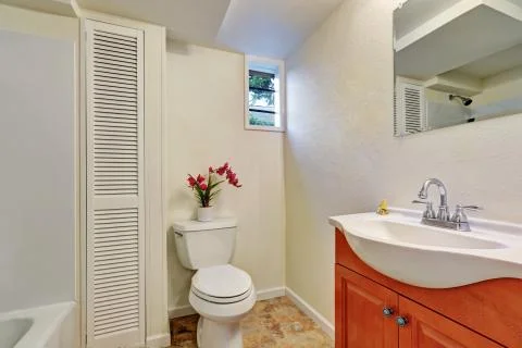 White classic bathroom interior with storage unit, small window and red flowe Stock Photos