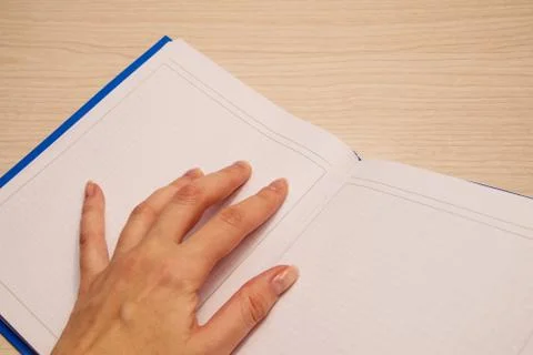 White clean notebook in a cage with a woman's left hand on it against a woode Stock Photos