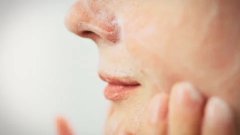 White cleansing foam spreads across young womans face in bright bathroom her Stock Footage 336570608