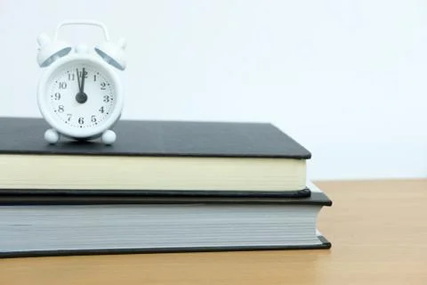 White clock above book stack on wooden table Stock Photos