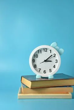 White clock with a bow on a stack of books on a blue background. Stock Photos