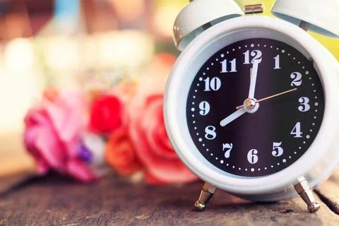 White clock with flowers on a table in muted vintage retro style. Stock Photos