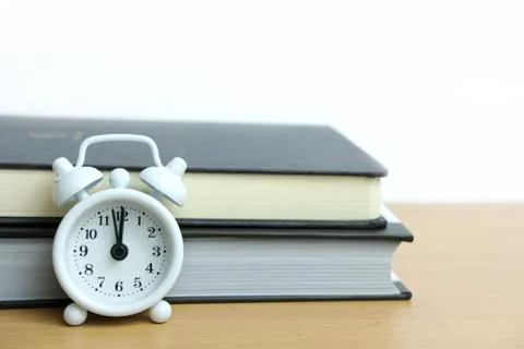 White clock in front of book above wooden table Foto stock