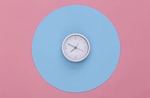 White clock on pink background with a blue circle. Conceptual studio shot. Mi Foto stock