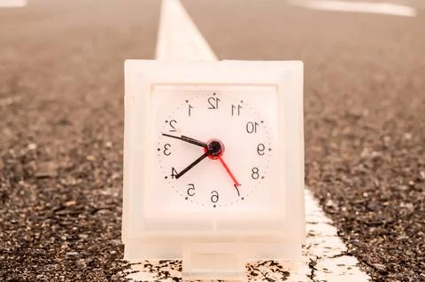 A white clock with red hands sits on a road Stock Photos
