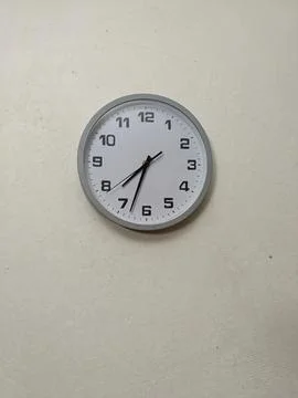A white clock on a white wall with black hands Stock Photos