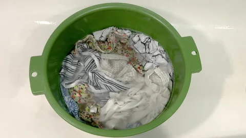 White clothes soaking in soapy water inside a green plastic basin Stock Footage 341510344