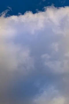 White cloud on the blue sky in the rays of the evening sun, close-up, vertica Stock Photos