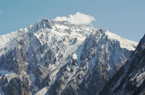 A white cloud next to a snow covered mountain peak. Stock Photos