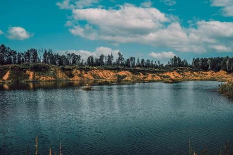 White clouds on a background of blue sky over a lake surrounded by trees Stock Photos