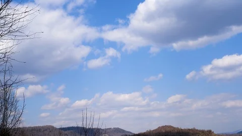White clouds on a blue sky against trees and mountains in early spring Stock Footage 111144916
