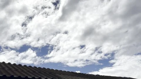 White Clouds Drifting Over a Rooftop in Blue Sky Stock Footage 338372310
