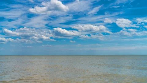 White clouds float across the blue sky above the sea Stock-Fotos