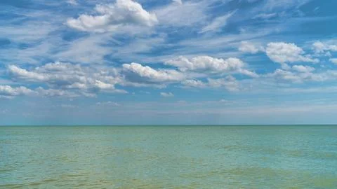 White clouds float across the blue sky above the sea Stock Photos
