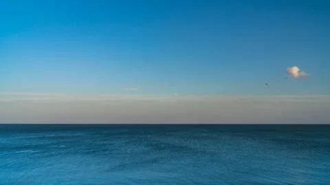 White clouds float across the blue sky above the sea Stock Photos