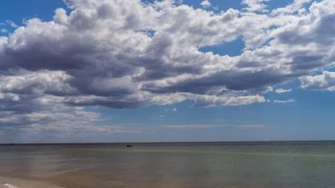 White clouds float across the blue sky above the sea Stock Photos