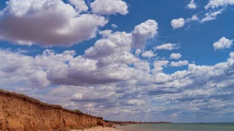 White clouds float across the blue sky above the sea Stock Photos