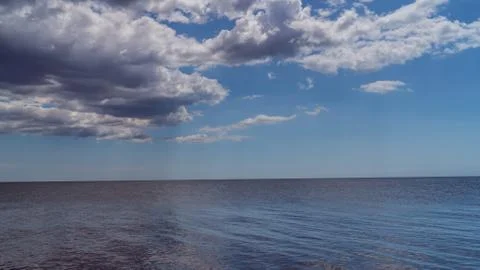 White clouds float across the blue sky above the sea Stock Photos