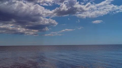 White clouds float across the blue sky above the sea Stock Photos