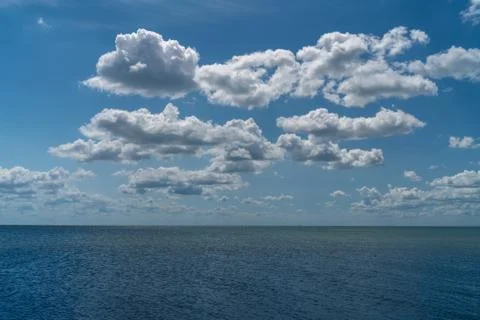 White clouds float across the blue sky above the sea Stock Photos