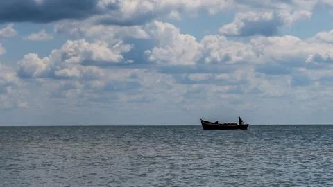 White clouds float across the blue sky above the sea Stock Photos