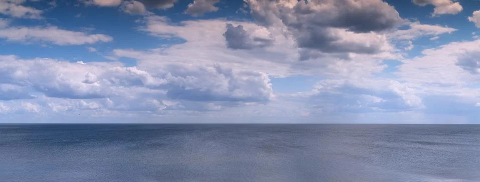 White clouds float across the blue sky above the sea-Pano Stock Photos