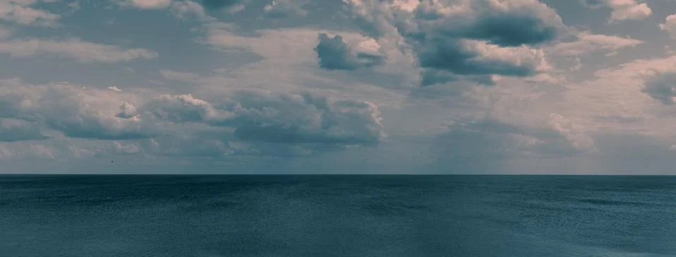 White clouds float across the blue sky above the sea-Pano Stock Photos