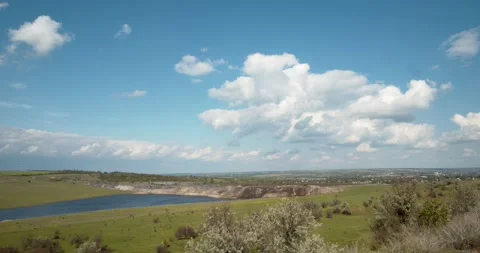 White clouds float over a green meadow and lake in the blue sky. Stock Footage 130741877