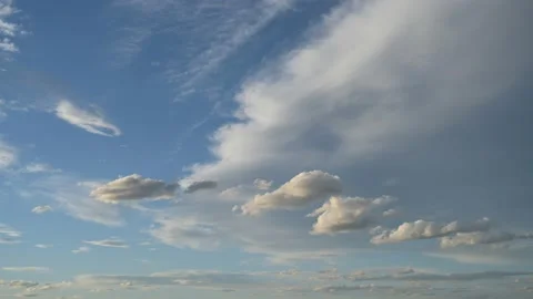White clouds with a hint of evening light drift through a blue sky in this clip Stock Footage 155352310