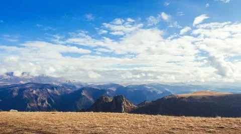 White clouds illuminated by the sun float over the mountain valley. View from Stock Photos