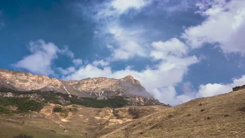 White clouds move against a blue sky over a mountain slope Stock Footage 152844324