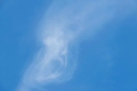 White clouds shaped like screaming head on blue sky background. Stock Photos